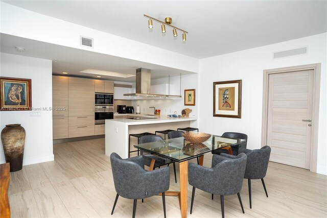 kitchen featuring kitchen peninsula, ventilation hood, black electric stovetop, light brown cabinetry, and a kitchen bar