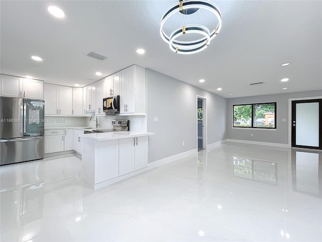 kitchen with a chandelier, sink, white cabinets, kitchen peninsula, and appliances with stainless steel finishes