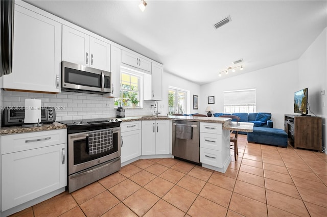 kitchen featuring tasteful backsplash, white cabinets, lofted ceiling, stainless steel appliances, and light tile patterned floors