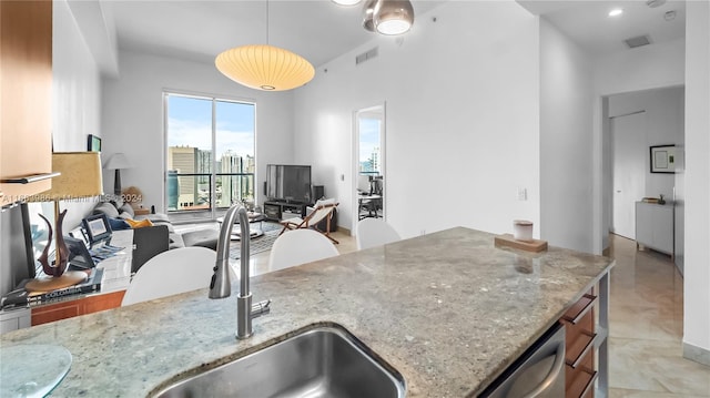 kitchen with pendant lighting, sink, light tile patterned floors, light stone countertops, and stainless steel dishwasher