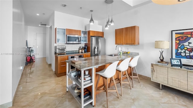 kitchen featuring appliances with stainless steel finishes, a breakfast bar, tasteful backsplash, decorative light fixtures, and sink