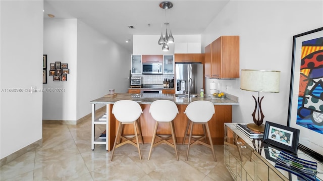 kitchen with light stone counters, hanging light fixtures, backsplash, stainless steel appliances, and a breakfast bar