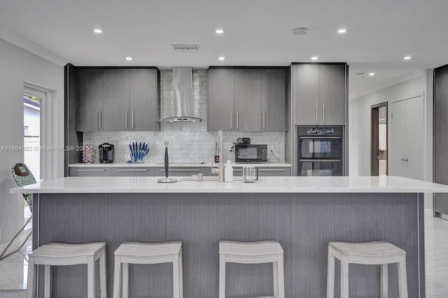 kitchen with black appliances, a kitchen breakfast bar, wall chimney exhaust hood, and gray cabinets