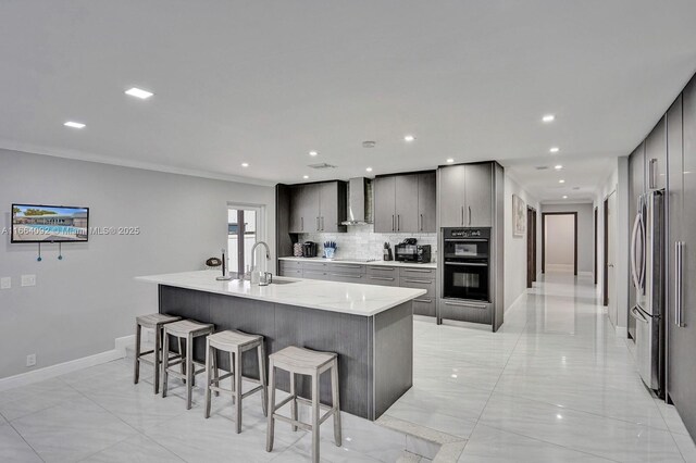 kitchen featuring light stone counters, wall chimney range hood, gray cabinetry, backsplash, and appliances with stainless steel finishes