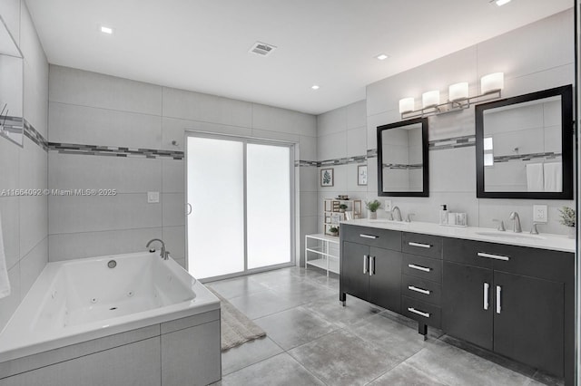 full bath featuring visible vents, a jetted tub, tile walls, and a sink