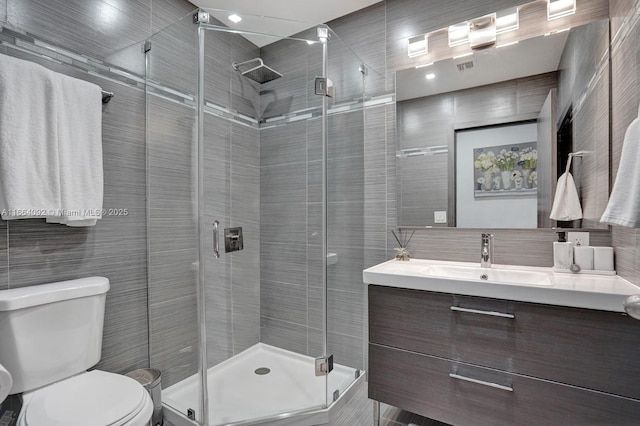 full bath featuring tile walls, a stall shower, toilet, and vanity