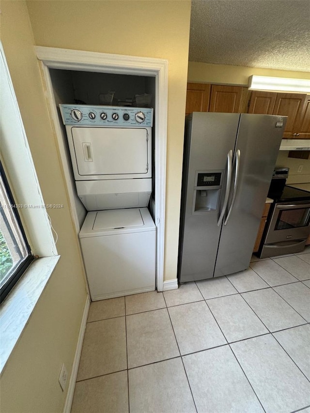 laundry area featuring a textured ceiling, stacked washer / dryer, and light tile patterned floors