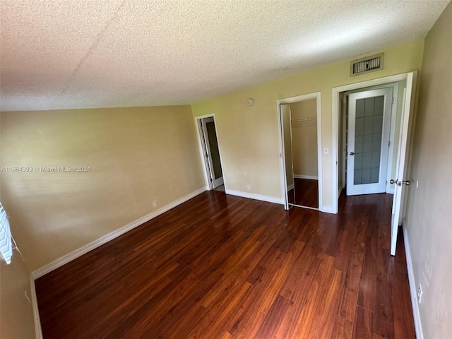 unfurnished bedroom featuring a textured ceiling, a spacious closet, dark hardwood / wood-style floors, and a closet