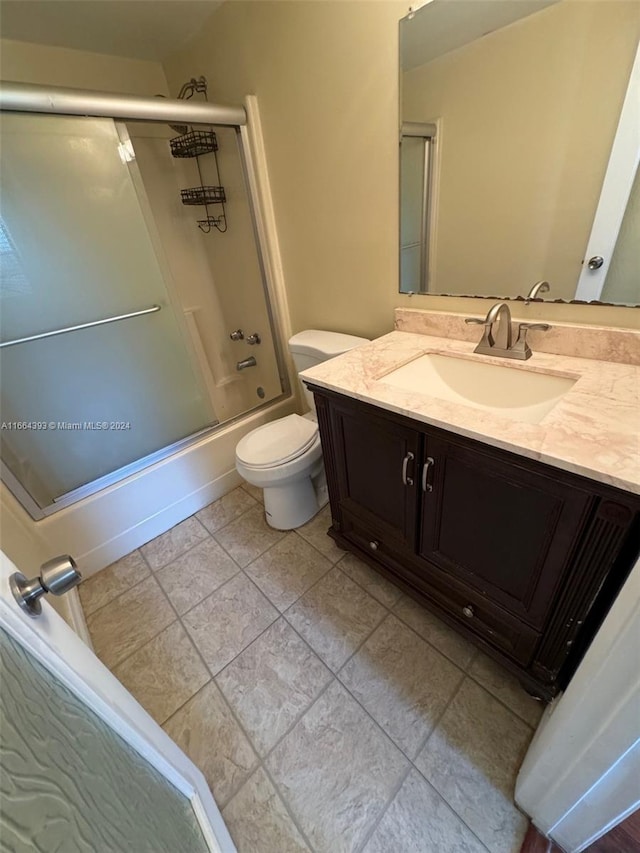 full bathroom with combined bath / shower with glass door, vanity, toilet, and tile patterned flooring