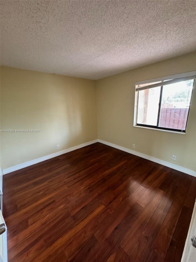 empty room with a textured ceiling and dark hardwood / wood-style flooring