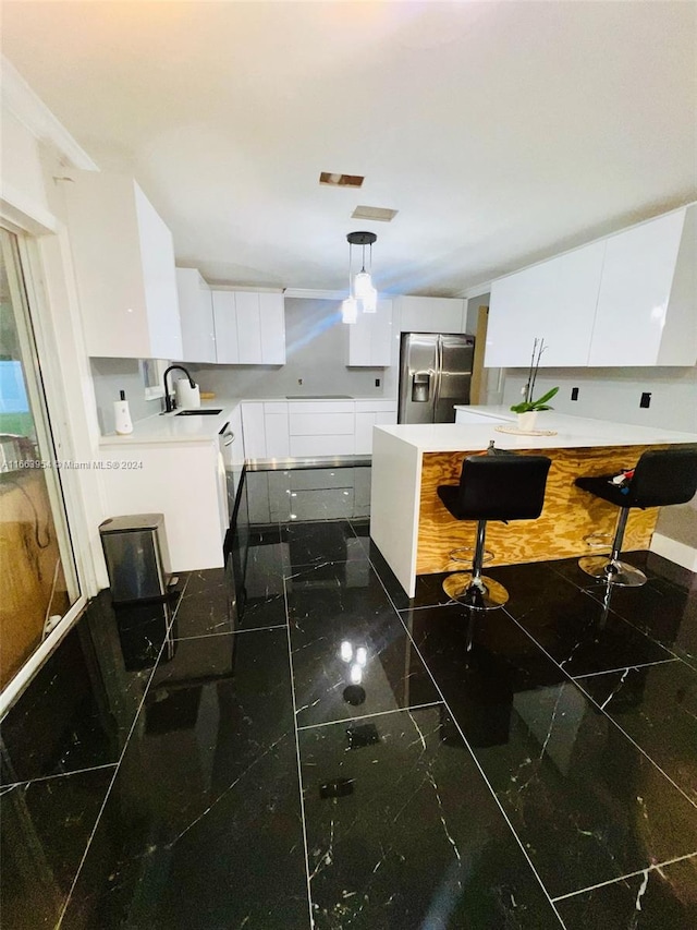 kitchen featuring a kitchen breakfast bar, stainless steel fridge, white cabinets, pendant lighting, and sink