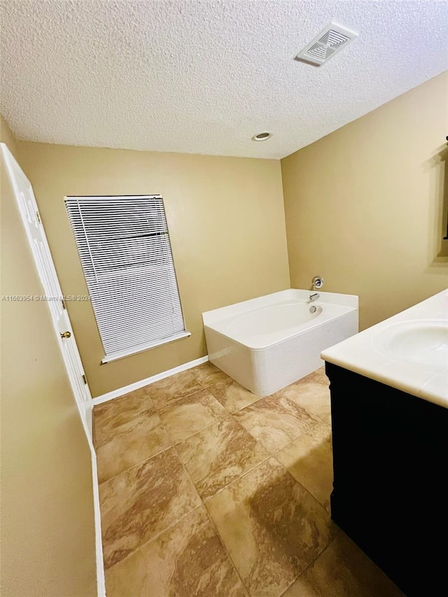 bathroom featuring vanity, a textured ceiling, and a tub