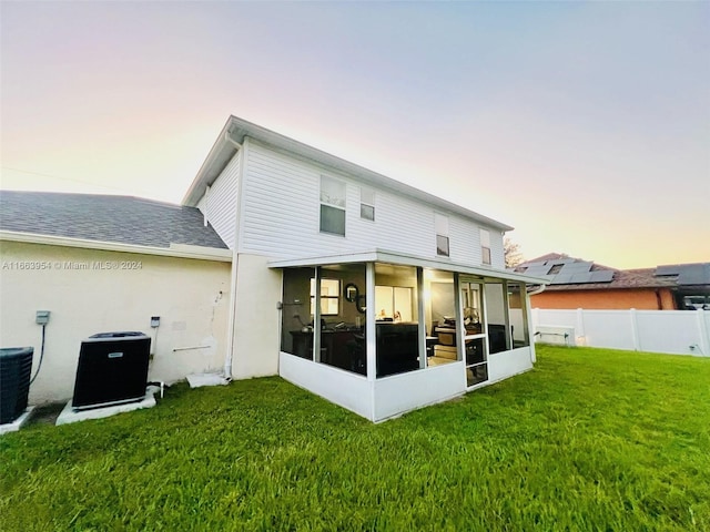 back house at dusk with a lawn, a sunroom, and central AC unit