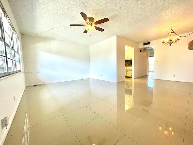 tiled empty room with a textured ceiling, ceiling fan with notable chandelier, and a wealth of natural light