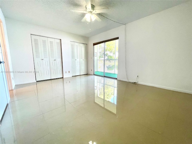 unfurnished bedroom featuring ceiling fan, access to outside, light tile patterned floors, a textured ceiling, and two closets