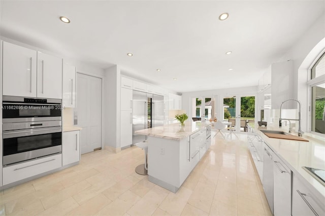 kitchen featuring sink, a kitchen island, double oven, white cabinets, and french doors