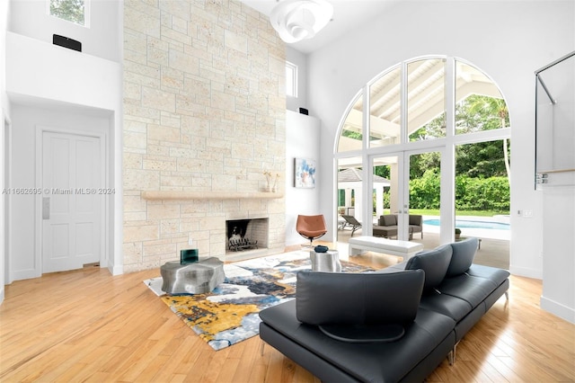 living room featuring a high ceiling, a stone fireplace, and light hardwood / wood-style flooring