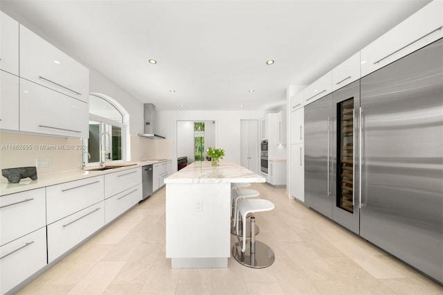 kitchen with wall chimney range hood, white cabinetry, a breakfast bar, and a kitchen island