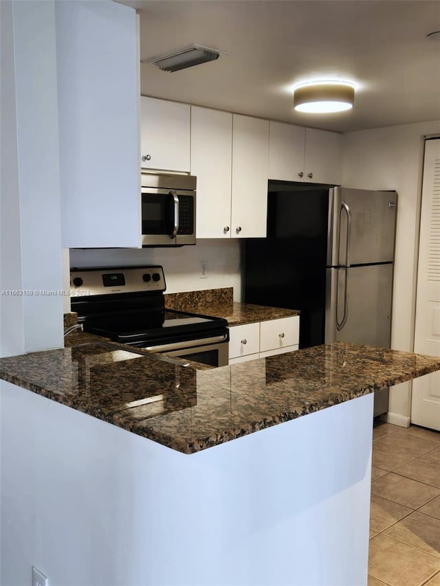 kitchen featuring dark stone counters, white cabinets, kitchen peninsula, stainless steel appliances, and light tile patterned floors