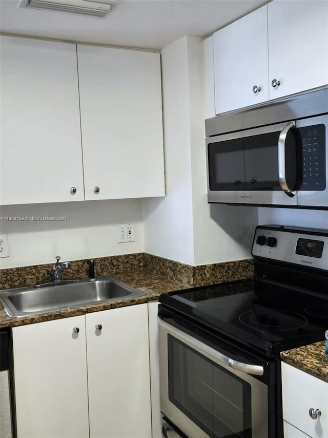 kitchen with dark stone countertops, stainless steel appliances, sink, and white cabinetry