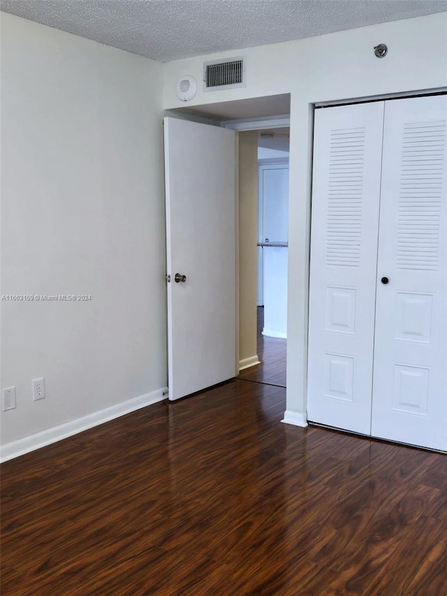 unfurnished bedroom featuring a closet, a textured ceiling, and dark hardwood / wood-style floors