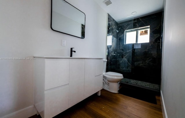 bathroom with vanity, toilet, a tile shower, and hardwood / wood-style flooring