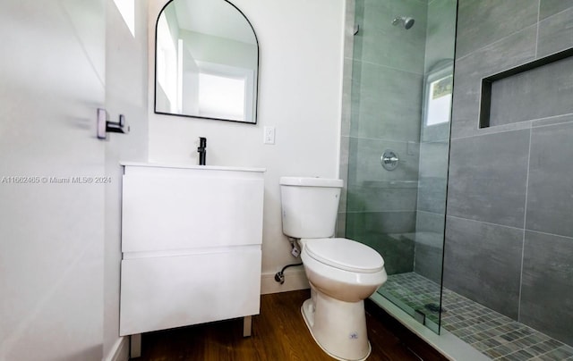 bathroom with wood-type flooring, vanity, toilet, and tiled shower