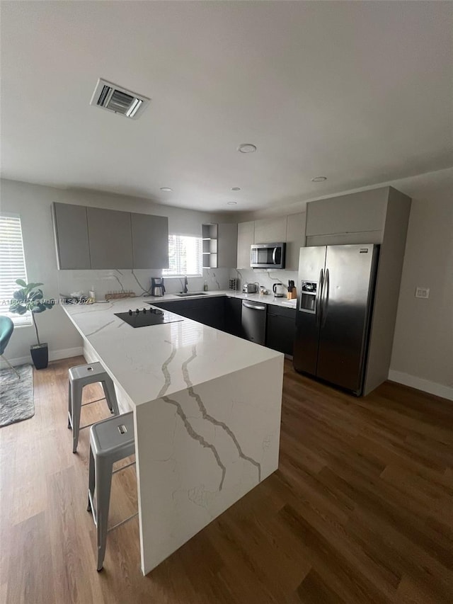 kitchen with gray cabinets, a breakfast bar area, stainless steel appliances, and light stone counters