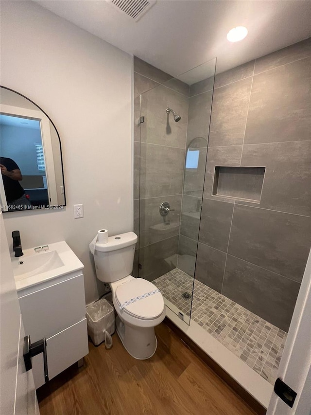 bathroom featuring toilet, vanity, hardwood / wood-style floors, and tiled shower