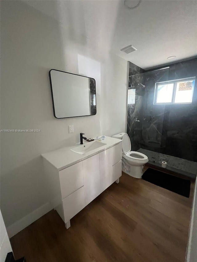 bathroom featuring vanity, hardwood / wood-style floors, toilet, and tiled shower