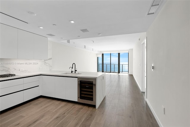 kitchen featuring sink, beverage cooler, white cabinetry, kitchen peninsula, and light hardwood / wood-style flooring