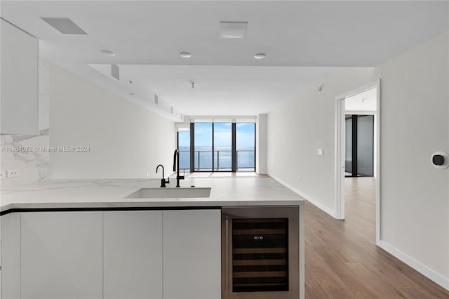 interior space with light wood-type flooring, wine cooler, sink, white cabinets, and expansive windows