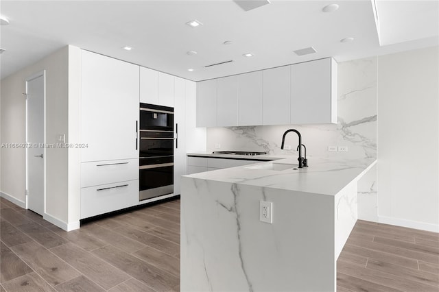 kitchen with sink, backsplash, light hardwood / wood-style floors, and white cabinetry