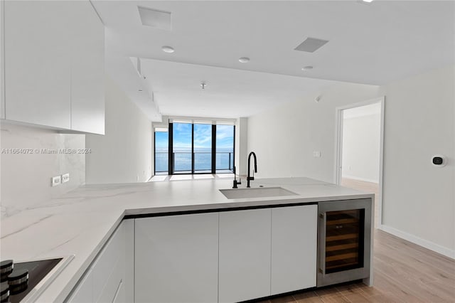 kitchen featuring black electric cooktop, white cabinetry, light wood-type flooring, beverage cooler, and sink