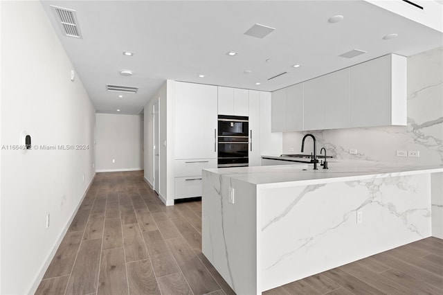 kitchen with light hardwood / wood-style flooring, white cabinetry, double oven, and tasteful backsplash