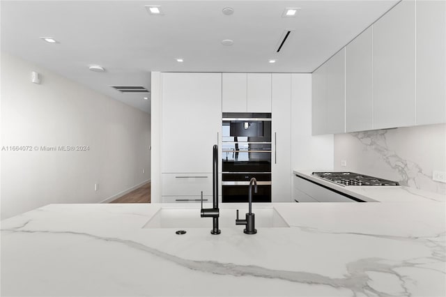 kitchen with light stone counters, white cabinets, black double oven, and stainless steel gas stovetop