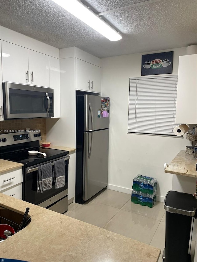 kitchen with white cabinetry, a textured ceiling, appliances with stainless steel finishes, and light tile patterned flooring