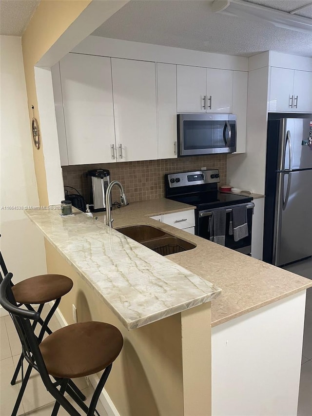 kitchen with appliances with stainless steel finishes, tasteful backsplash, a breakfast bar, white cabinets, and kitchen peninsula