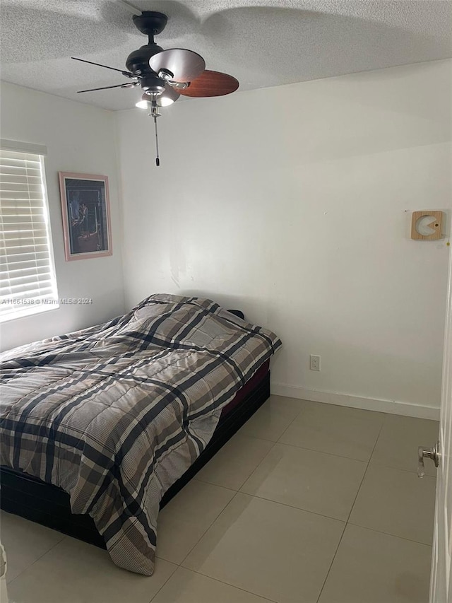 bedroom featuring ceiling fan, light tile patterned floors, and a textured ceiling