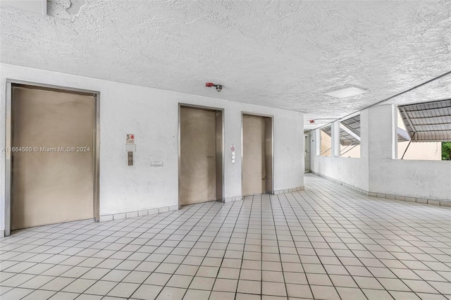 tiled empty room with a textured ceiling and elevator