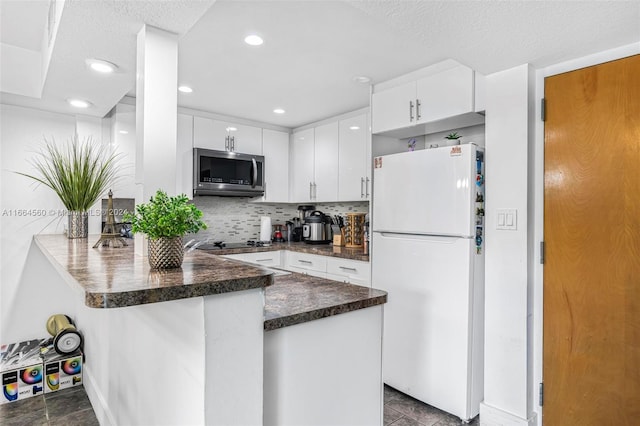 kitchen with decorative backsplash, kitchen peninsula, white cabinets, and white fridge