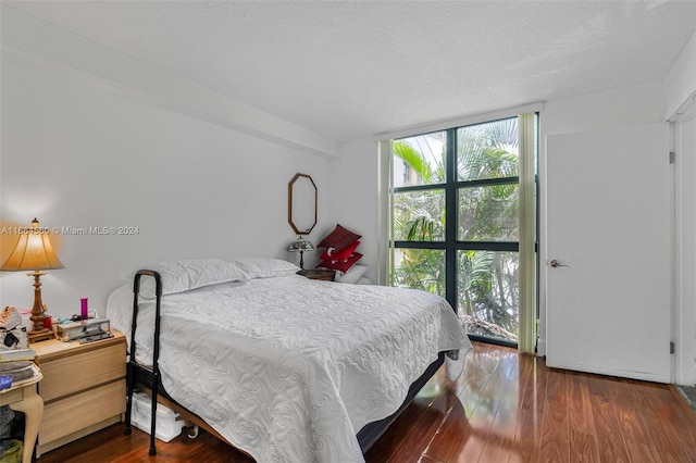 bedroom with a textured ceiling, a wall of windows, and dark hardwood / wood-style flooring