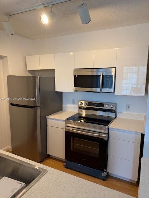 kitchen with light wood finished floors, stainless steel appliances, track lighting, white cabinetry, and light countertops