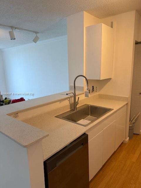 kitchen with a sink, white cabinets, light wood-type flooring, rail lighting, and dishwashing machine