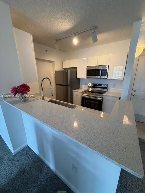 kitchen with light stone counters, rail lighting, a sink, stainless steel appliances, and white cabinets