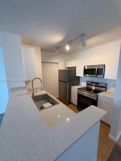 kitchen with a sink, white cabinetry, modern cabinets, track lighting, and appliances with stainless steel finishes