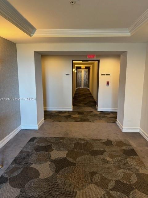 hallway featuring ornamental molding, dark colored carpet, and a raised ceiling