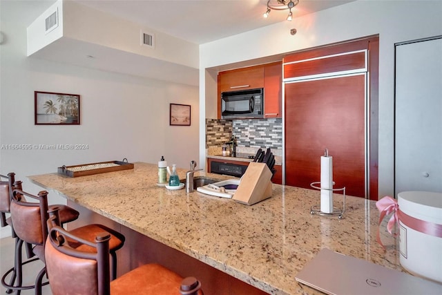 kitchen featuring a breakfast bar, light stone counters, paneled built in fridge, and tasteful backsplash