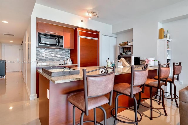 kitchen featuring light stone countertops, a kitchen bar, kitchen peninsula, and decorative backsplash