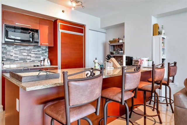 kitchen featuring decorative backsplash, light stone counters, and a breakfast bar area